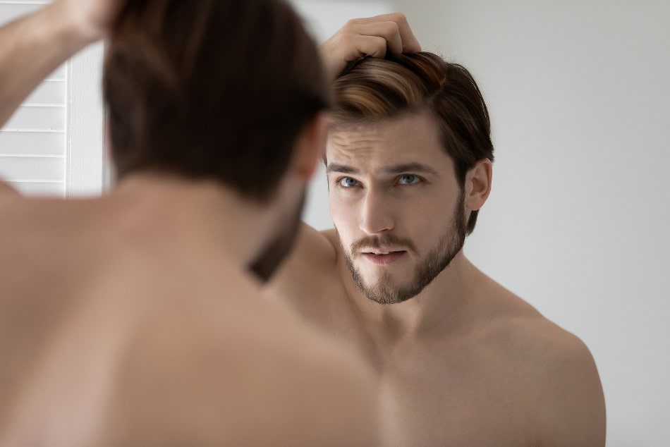 Mann mit einer Haar-Heterochromie inspiziert seine Haare vor dem Spiegel 