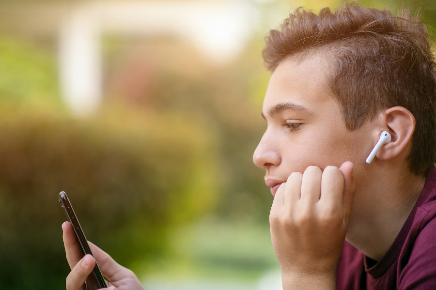 Junge leidet unter Haarausfall in der Pubertät und schaut traurig auf sein Handy