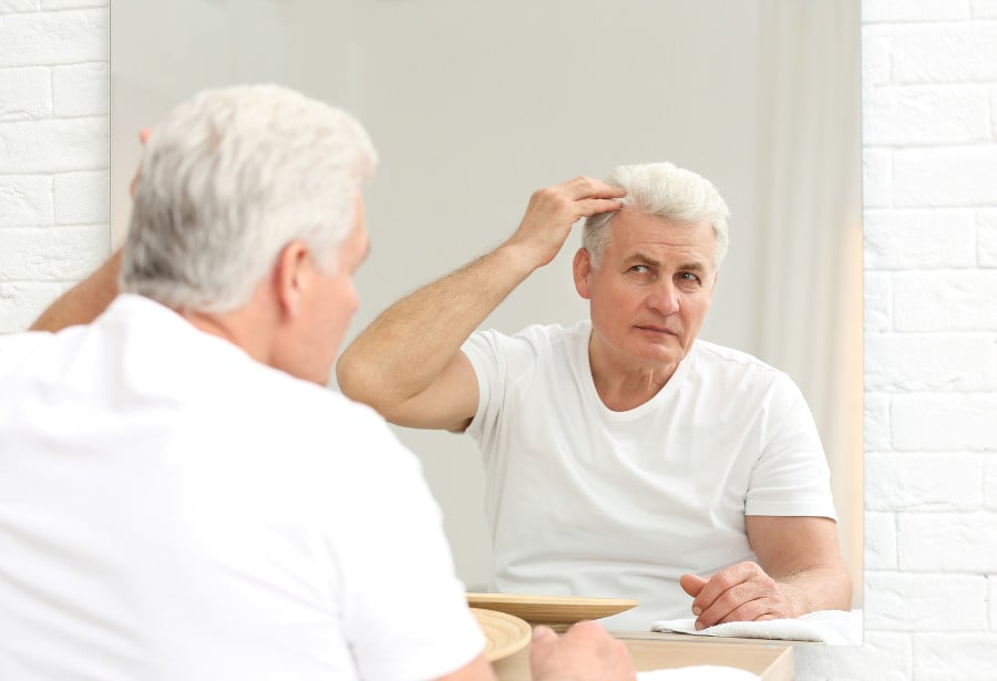 Mann kontrolliert Haarwuchs im Spiegel nach einer Haartransplantation und fragt sich, ob zwei Sitzungen nötig sind