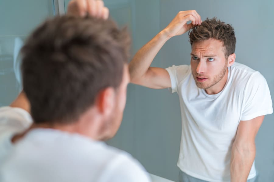 Mann vor dem Spiegel fasst sich fragend in die Haare wegen Haartransplantation Langzeitergebnisse