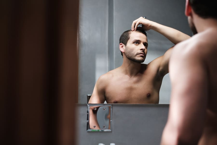 Mann vor Spiegel überlegt was vor Haartransplantation zu beachten ist