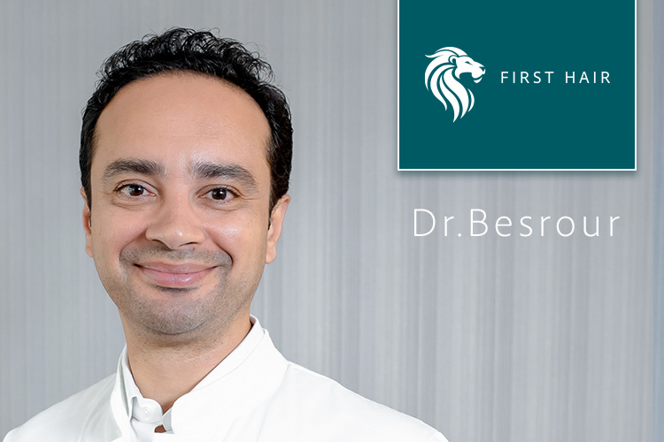Dr Besrour lächelnd vor einem grauen Hintergrund