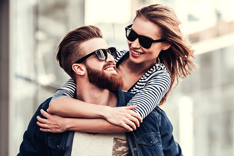 Junges Paar mit Sonnenbrillen umarmt sich vor Bürokomplex