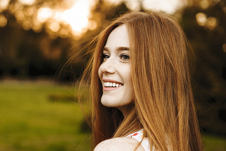Lächelnde Frau mit roten langen Haaren draußen in der Natur